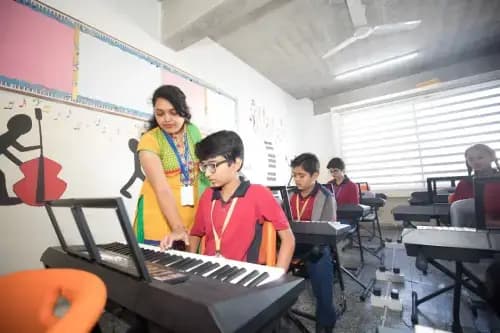 Students learning to play the keyboard in a music class with a teacher guiding them.