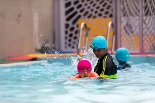 Swimming instructor guiding a young girl in the pool, teaching her basic swimming techniques with hands-on support.